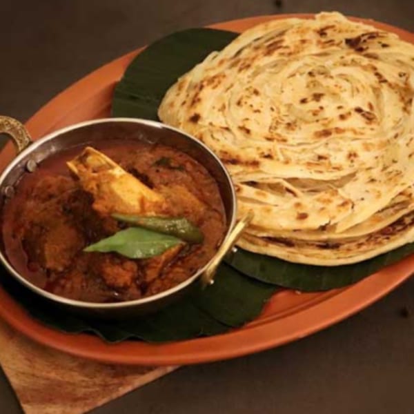 Indian lamb curry with bone-in meat, green chilies, and a stack of paratha bread on a plate.