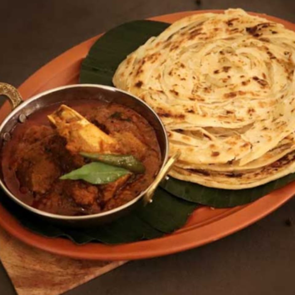 Indian lamb curry with bone-in meat, green chilies, and a stack of paratha bread on a plate.