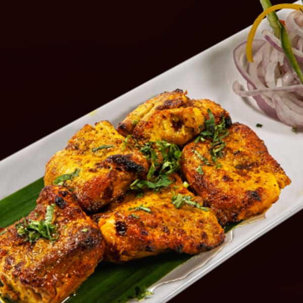 Indian chicken tikka pieces garnished with cilantro, served on a banana leaf with sliced onions.