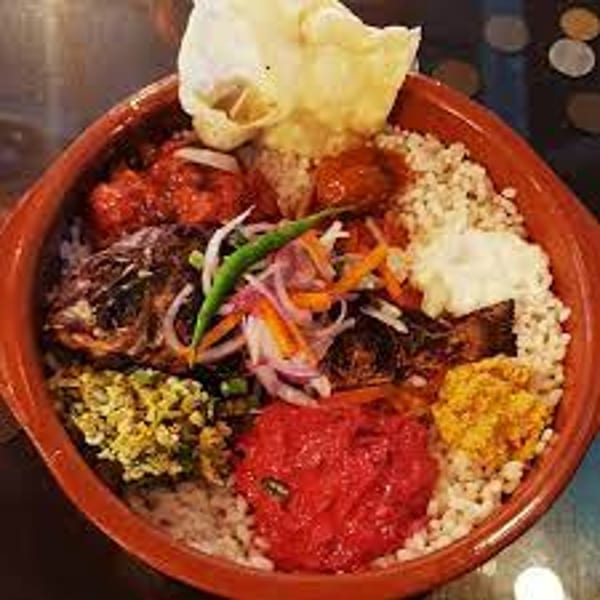 A vibrant Indian thali with rice, fish, papadum, and various colorful curries in a clay pot.